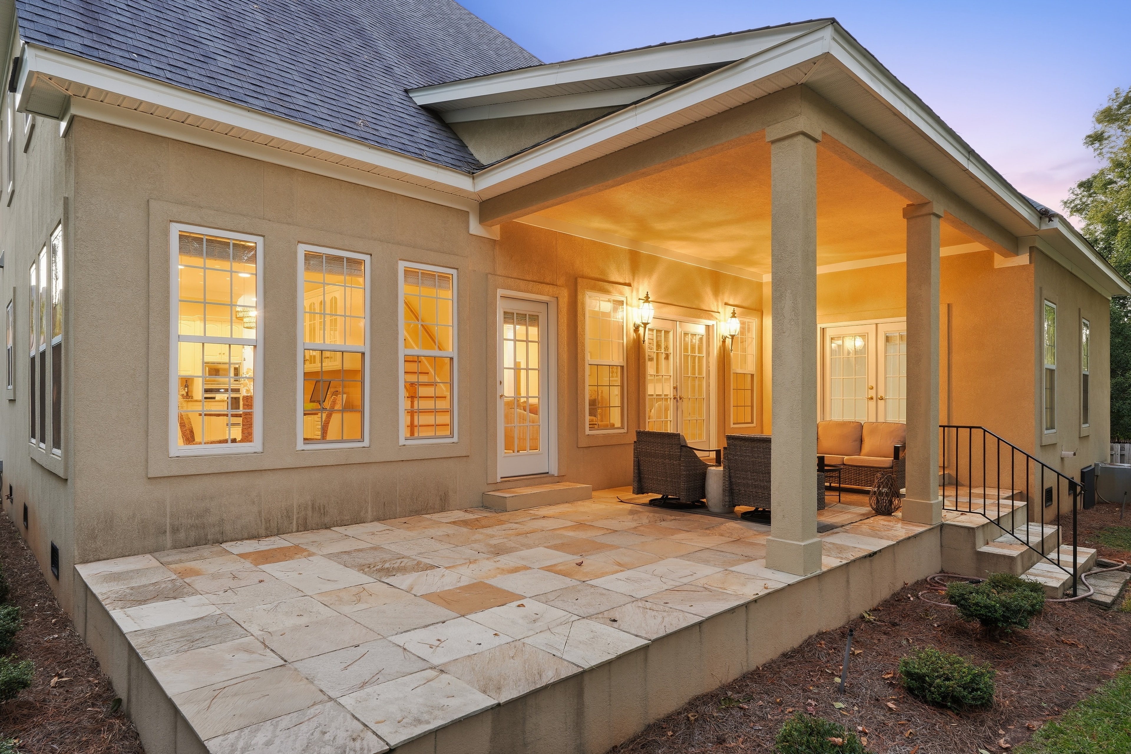 Covered stone patio at dusk with warm sconces and outdoor seating