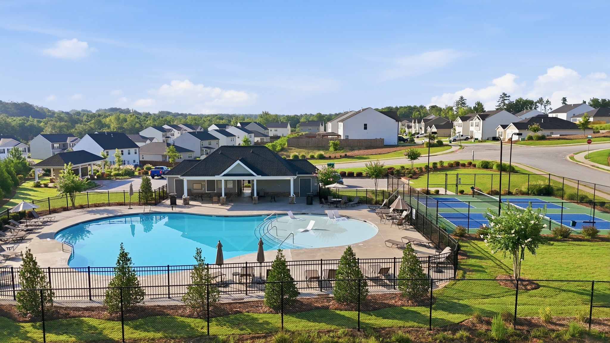 Aerial view of a community pool, clubhouse, and pickleball courts