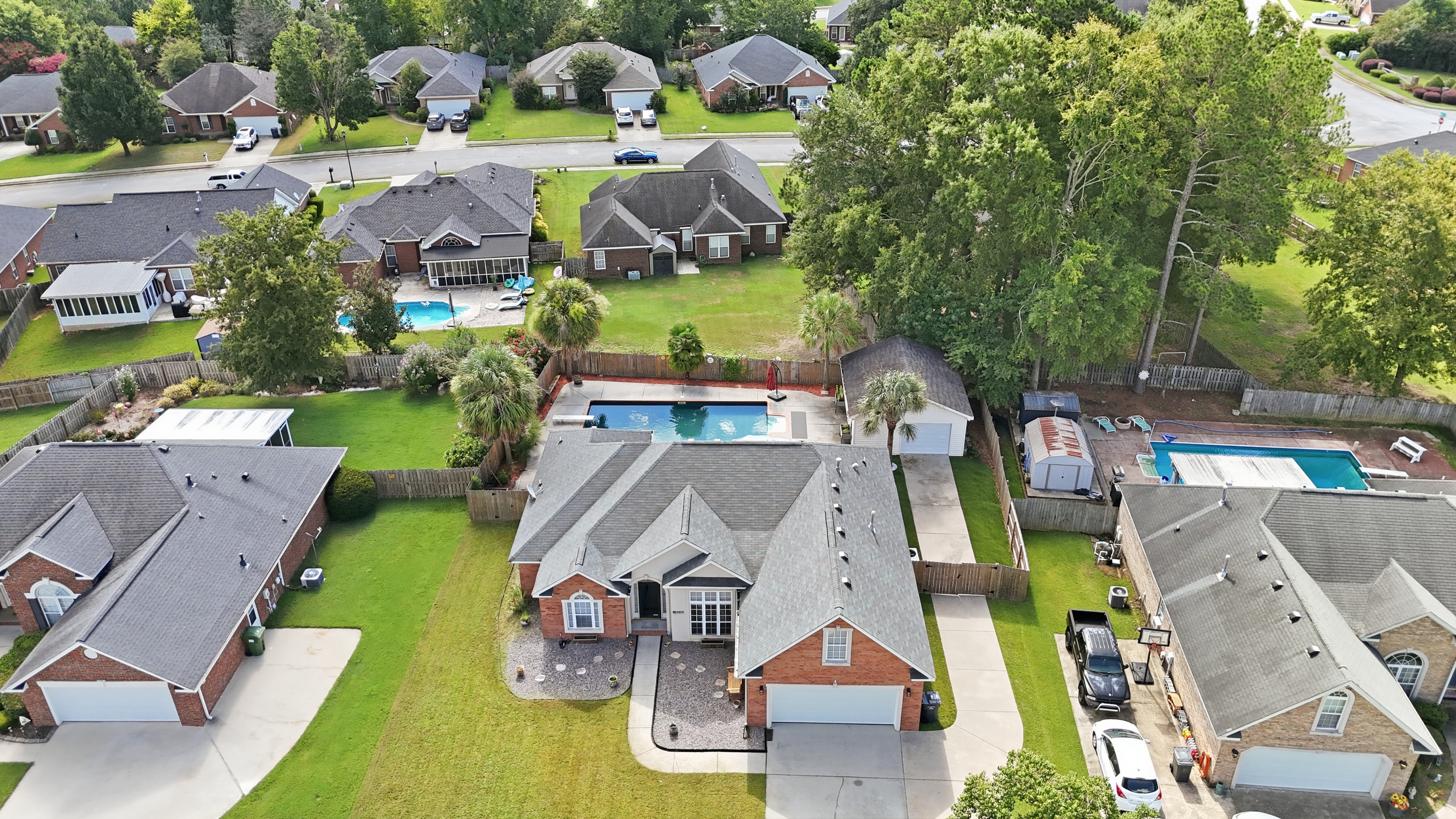 Drone view of a brick home with a backyard pool in an established neighborhood
