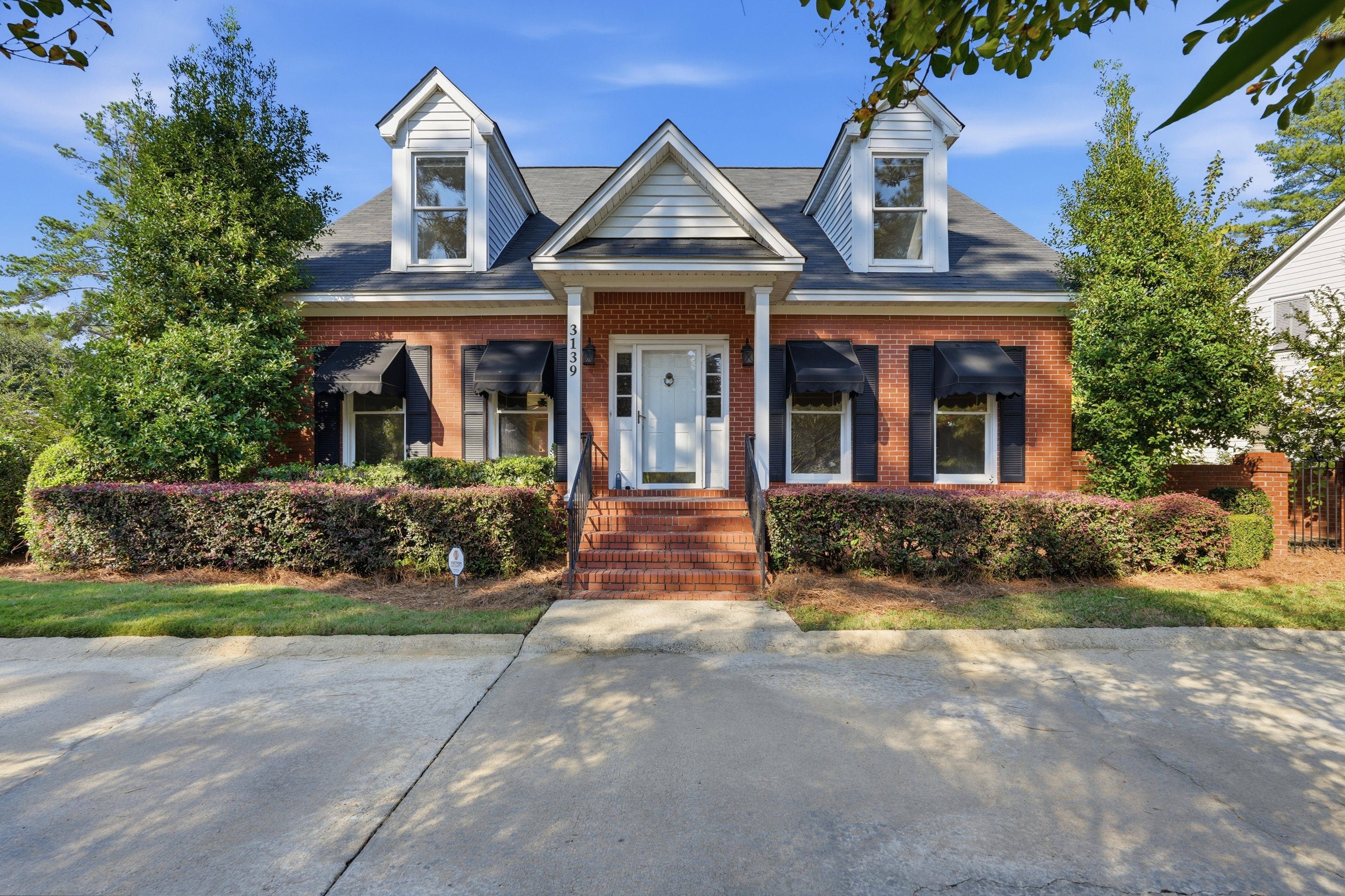 Red brick Cape Cod home with black awnings, dormers, and a brick front walk