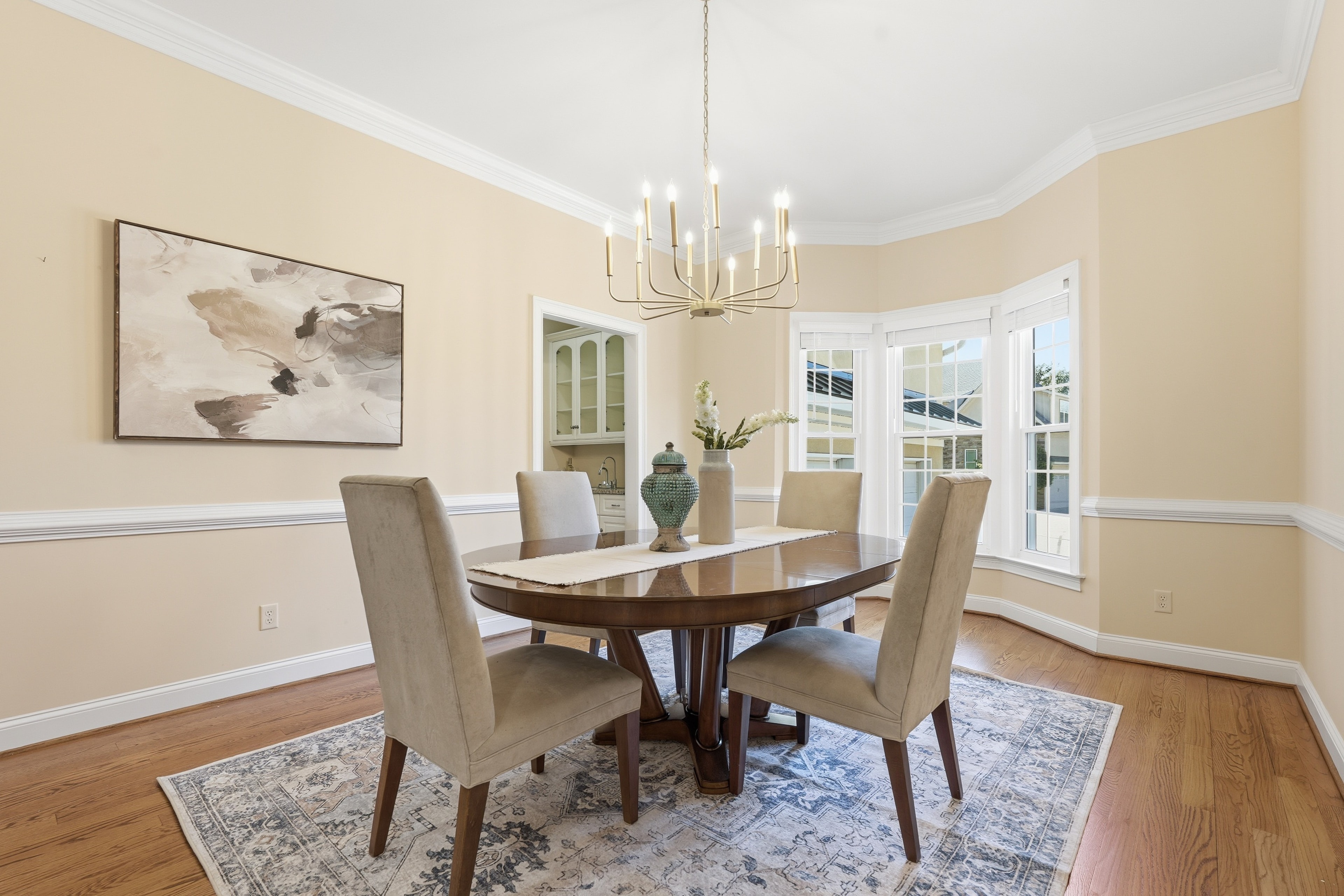 Dining room with a brass chandelier, oval table, upholstered chairs, and a bay window