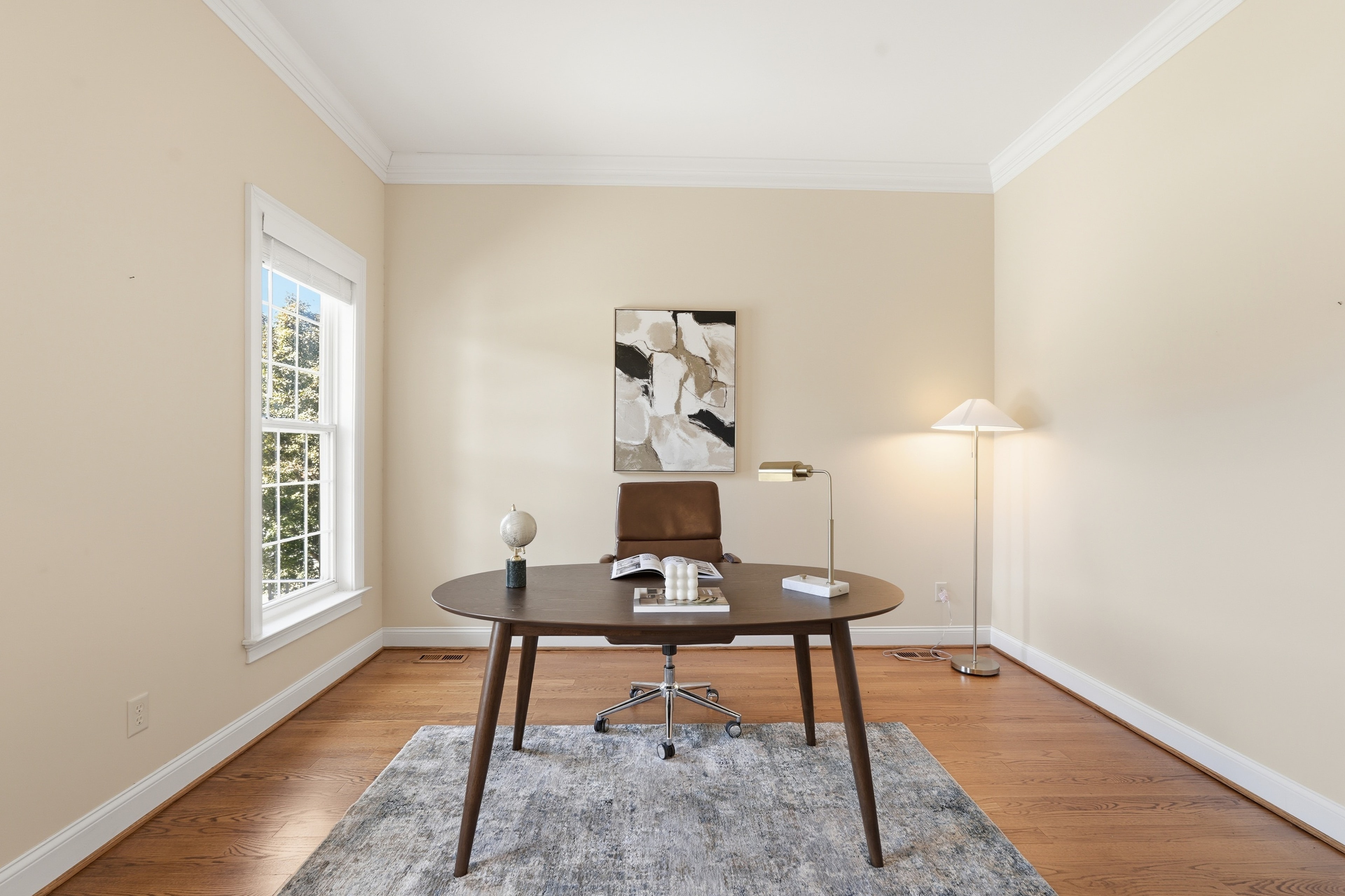 Home office with a walnut desk, leather chair, brass lamp, and abstract art