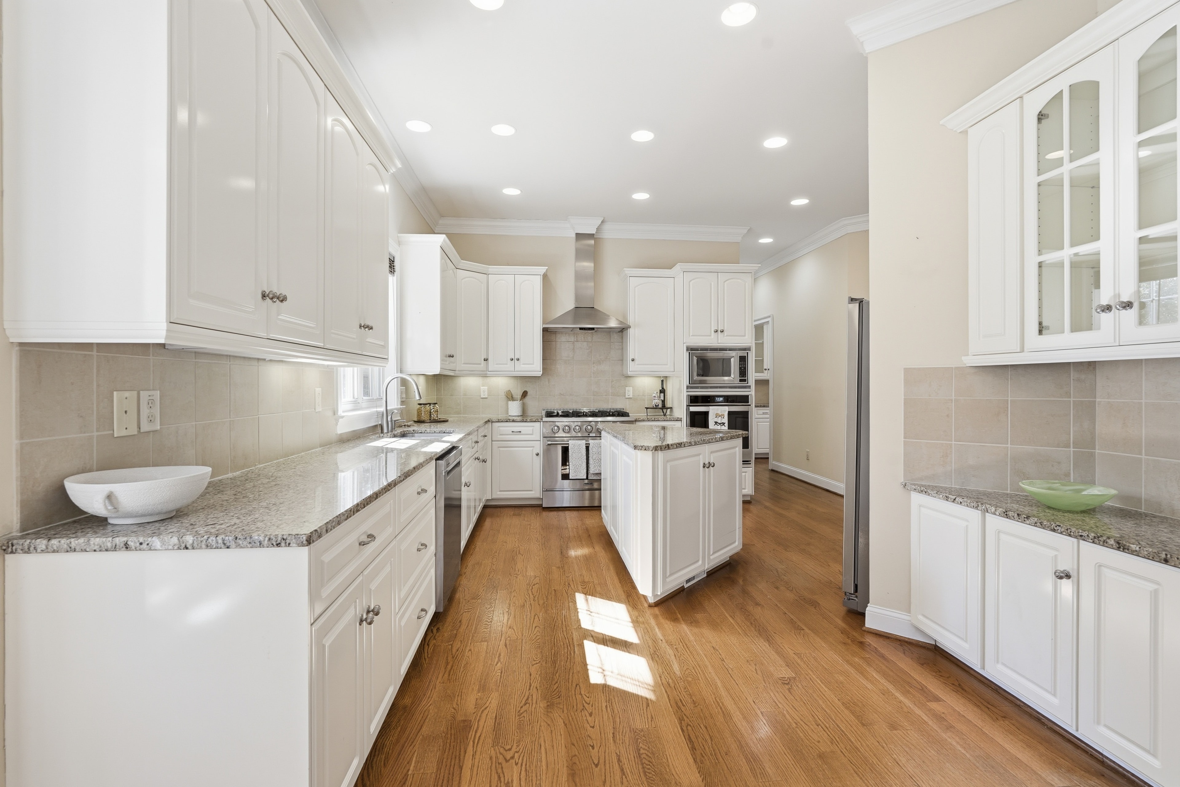 Bright white kitchen with granite counters, a center island, and sunlight across oak floors